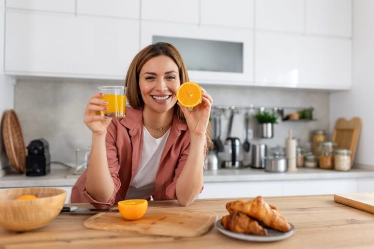 Beautiful young woman drinking fresh orange juice in kitchen